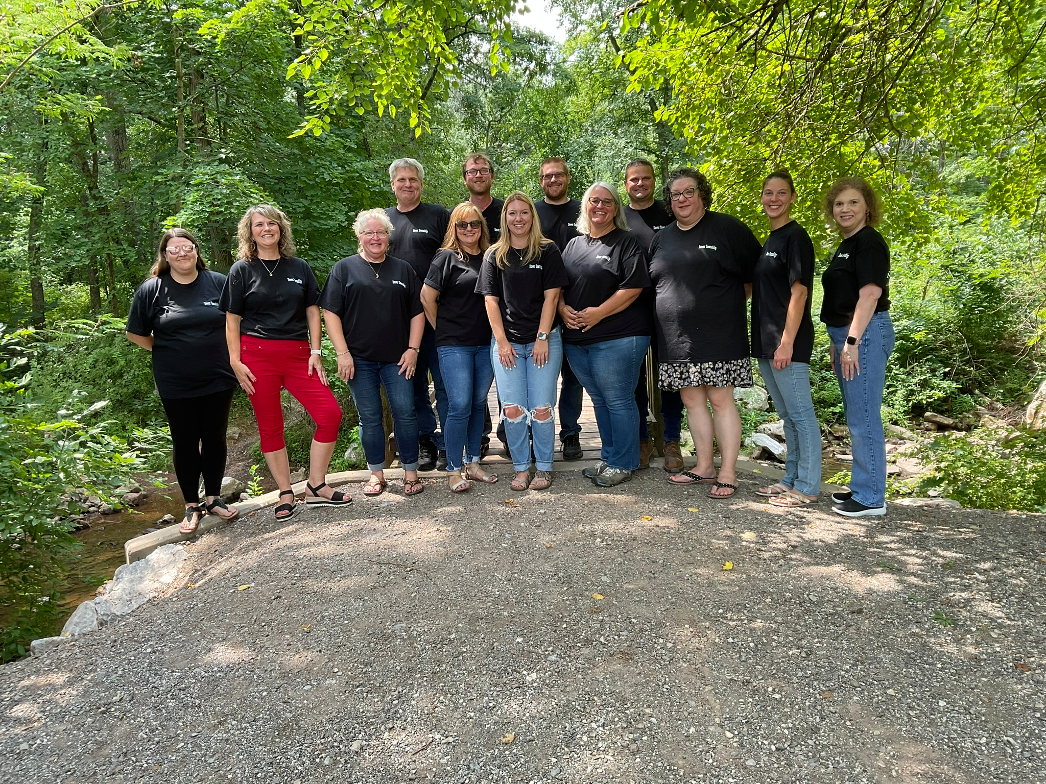 A group photo of the Administration staff of Dover Township. All the employees are wearing black T-shirts and standing by the bridge at Brookside Park.